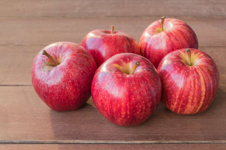 five red apples on wooden table closeup view