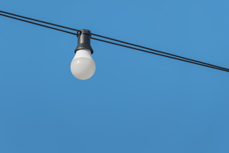 Wired light bulb hanging over blue sky in summer outdoorsの写真素材