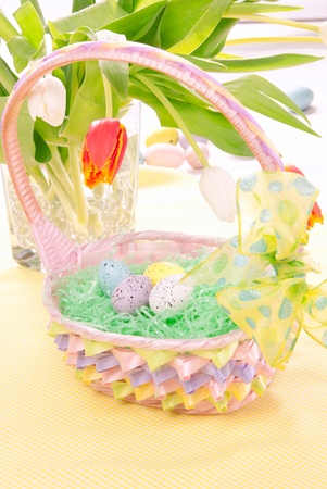 Easter Painted Colorful eggs in pink basket for Shristian sunday morning decorated with spring tulips on a pastel color backgroundの写真素材