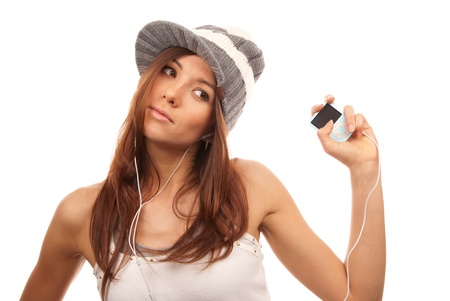 Beautiful young woman listening to dance music on mp3 player in headphones wearing hip-hop style hat and top, isolated on white backgroundの写真素材