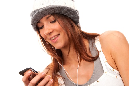 Pretty young teenage girl typing and reading text message on her new modern cell phone mobile and listening music in headphones isolated on a white backgroundの写真素材