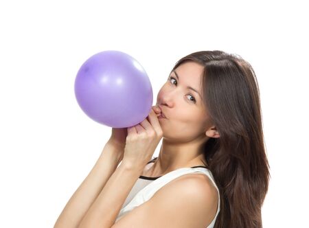 Young happy girl blowing balloons for birthday party smiling and looking at the camera on a white backgroundの写真素材