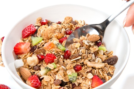 Muesli cereals bowl and spoon with almond, pine nuts, walnut, raisins, oat and wheat flakes, sultanas, fresh fruits kiwi, strawberry pieces, banana, pomegranate seedsの写真素材