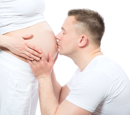 Portrait of young happy man kissing belly of his pregnant woman wife isolated on a white background