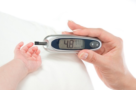 Doctor hand measuring glucose level blood test from diabetes patient child baby using glucometer and small drop of blood from finger and test strips isolated on a white backgroundの写真素材
