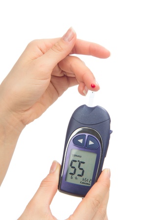 Diabetes patient measuring glucose level blood test using glucometer and small drop of blood from finger and test strips isolated on a white backgroundの写真素材