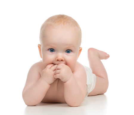 Infant child baby girl in diaper lying happy smiling and eating hands on a white backgroundの写真素材
