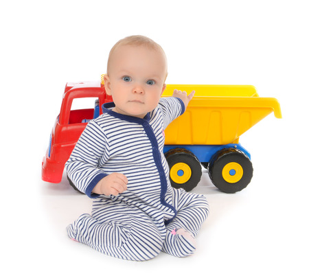 Cute child baby boy toddler happy sitting with big toy car truck red yellow and blue colors in hand on a white backgroundの写真素材