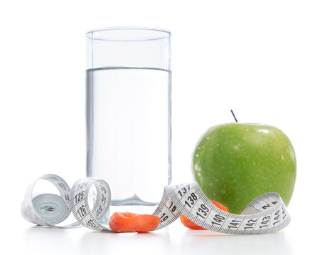 Dietting breakfast diabetes weight loss concept with tape measure organic green apple glass of drinking water and dried apricots on a white backgroundの写真素材