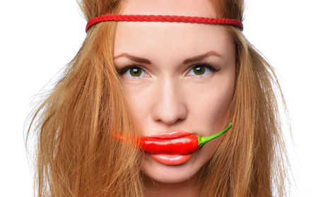 Closeup Fashion portrait of happy young woman placing bite red chili between in her mouth isolated on a white backgroundの写真素材