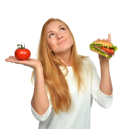 Fast food concept. Tasty unhealthy burger sandwich in hand and tomato getting ready to eat isolated on a white backgroundの写真素材