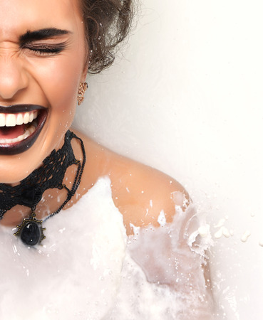 Closeup portrait of a sexy woman face laughing smiling in white milk bath with splashes creamの写真素材
