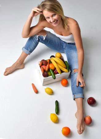 Pretty young woman near box with fresh organic vegetables and fruits smilingの写真素材
