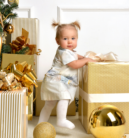 Christmas baby child toddler near gold christmas tree presents and ball decoration near present gift box. New Year 2016 holiday concept isolated on a white backgroundの写真素材