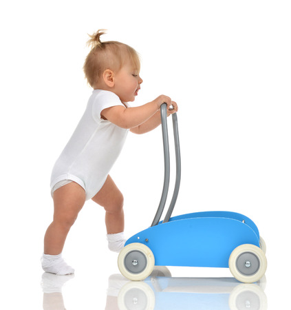 Cute smiling baby girl toddler with toy walker make first steps isolated on a white backgroundの写真素材