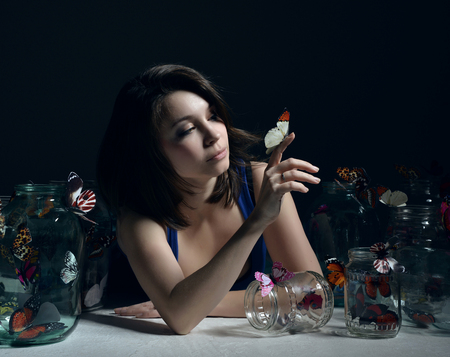 Beautiful fashion girl with butterflies in clear glass cans on a dark backgroundの写真素材