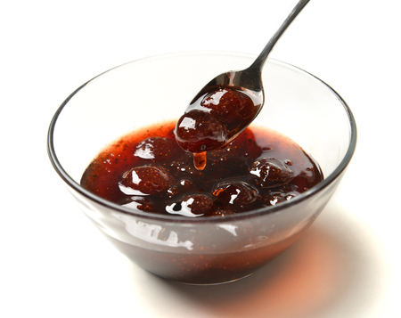Sweet strawberry jam in the transparent glass bowl with tea spoon on a white backgroundの写真素材