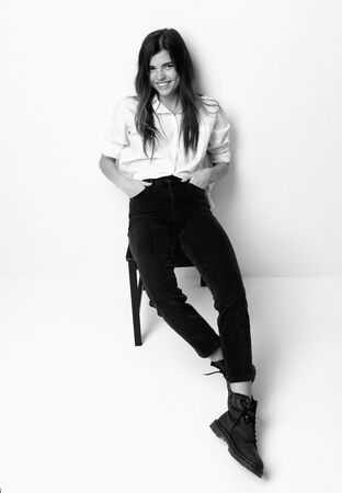 Young beautiful hipster girl sitting in white shirt and modern stylish boots happy smiling laughing black and white photoの写真素材