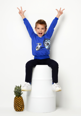 Happy young boy sitting in blue sweater thinking and looking up with big yellow clock pointing finger up on white backgroundの写真素材