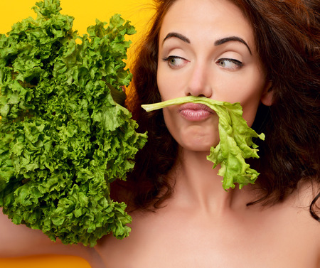 Healthy eating concept. Dieting. Woman hold lettuce looking at the corner on yellow  backgroundの写真素材
