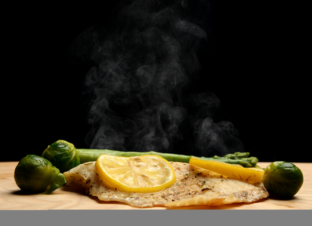 Hake white fish fillet with green asparagus brussel sprouts and lemon hot steam smoke on black...