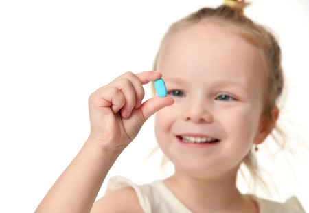 Young baby girl hold light blue headache  pill medicine tablet in small hand isolated on a white backgroundの写真素材
