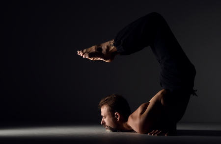 Old man practicing yoga scorpion pose asana on dark background
