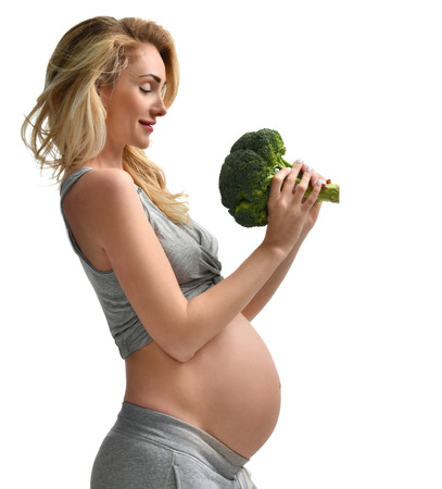 Beautiful pregnant woman big belly holding broccoli Pregnancy motherhood expectation healthy eating and weight control concept isolated on a white backgroundの写真素材