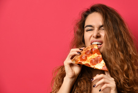 Young beautiful woman with slice of pepperoni pizza screaming laughing on dark pink backgroundの写真素材