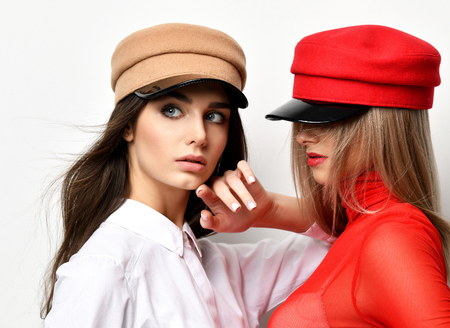 Two young fashion brunette woman in red and brown peaked cap together on grey backgroundの写真素材