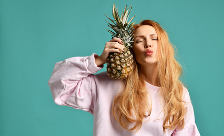 Young happy beautiful sexy woman kissing and holding pineapple fruit on a blue mint backgroundの写真素材