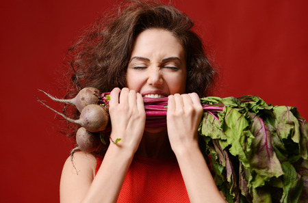 Young sport woman bite eat fresh beetroot with green leaves. Dieting. Healthy eating concept on red...