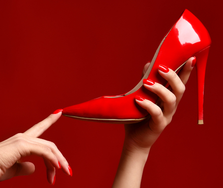 Woman hands hold red high hill shoe on dark red backgroundの写真素材