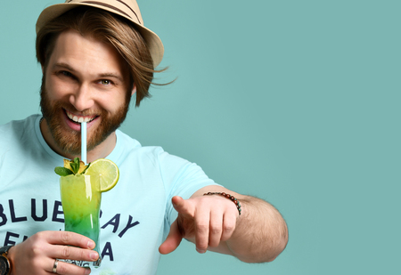 Young man in hat hold margarita cocktail drink juice happy smiling pointing one finger at the camera over blue mint backgroundの写真素材