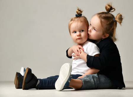 Beautiful little sisters sitting kissing together happy smiling on gray backgroundの写真素材