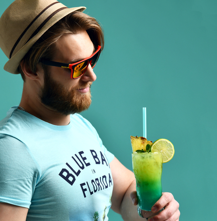 Young man in hat drinking margarita cocktail drink juice happy looking at camera over blue mint backgroundの写真素材