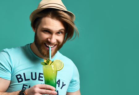 Young man in hat drinking margarita cocktail drink juice happy looking at camera over blue mint backgroundの写真素材