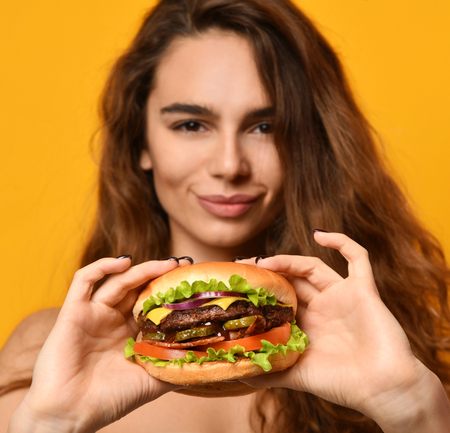 Woman eat burger sandwich with hungry mouth on yellow background. Closeup composition of Fast food concept.の写真素材