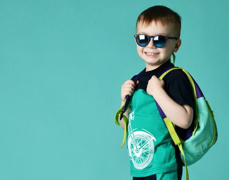Preschool boy kid standing with backpack and sunglasses in shorts and t-shirt on green mint...
