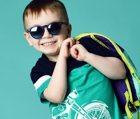 Preschool boy kid standing with backpack and sunglasses in shorts and t-shirt on green mint backgroundの写真素材