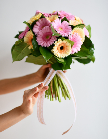 Beautiful woman hands hold bouquet of gerbera flowers pink and yellow on grey backgroundの写真素材