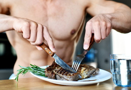 Man ready to eat cut with fork and knife grill beef steak and glass of water on a kitchen backgroundの写真素材