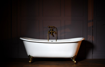 Beautiful classic style white claw foot bathtub with stainless steel old fashioned faucet and sprayer on dark backgroundの写真素材