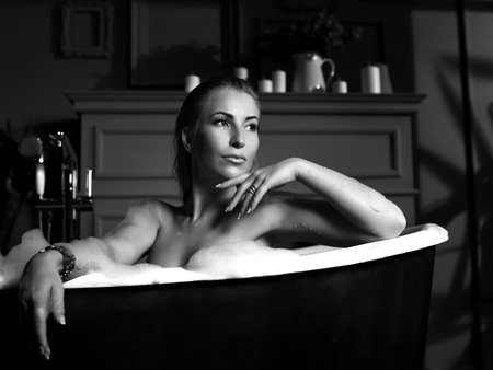 Young beautiful woman sitting in bathroom near expensive bathtub bath looking at the corner on dark backgroundの写真素材
