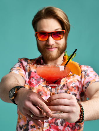 Young man in hat and sunglasses drinking margarita cocktail drink juice happy looking at camera laughing over light green backgroundの写真素材