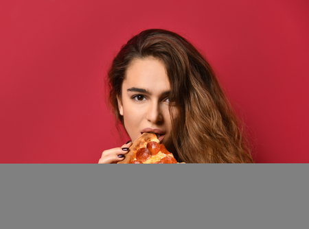 Young beautiful woman eat slice of pepperoni pizza with closed eyes smiling on red pink backgroundの写真素材
