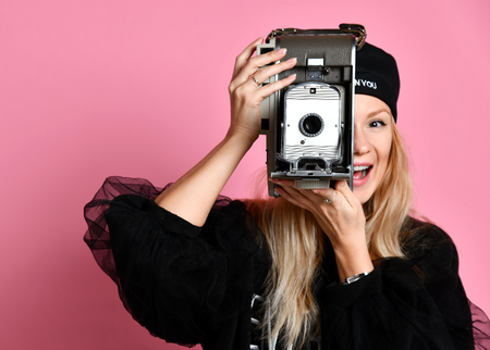 Young woman take photo use antique old portable photo camera medium frame on light pink backgroundの写真素材