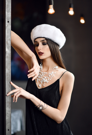 Beautiful woman in white winter fir hat cap  in expensive loft restaurant touching wall with fingerの写真素材