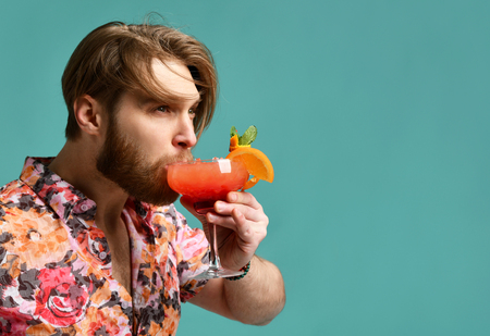 Young man drinking margarita cocktail drink juice happy looking at corner laughing over light blue mint backgroundの写真素材