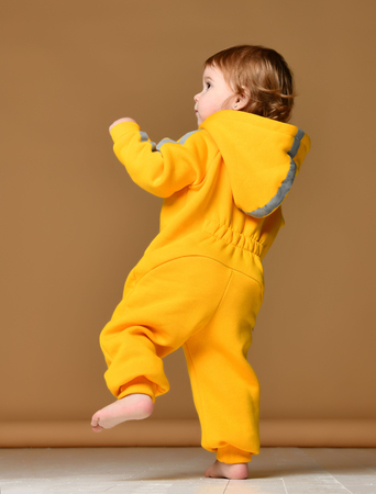 Infant child baby girl kid toddler in winter yellow overalls make first steps on grey  backgroundの写真素材